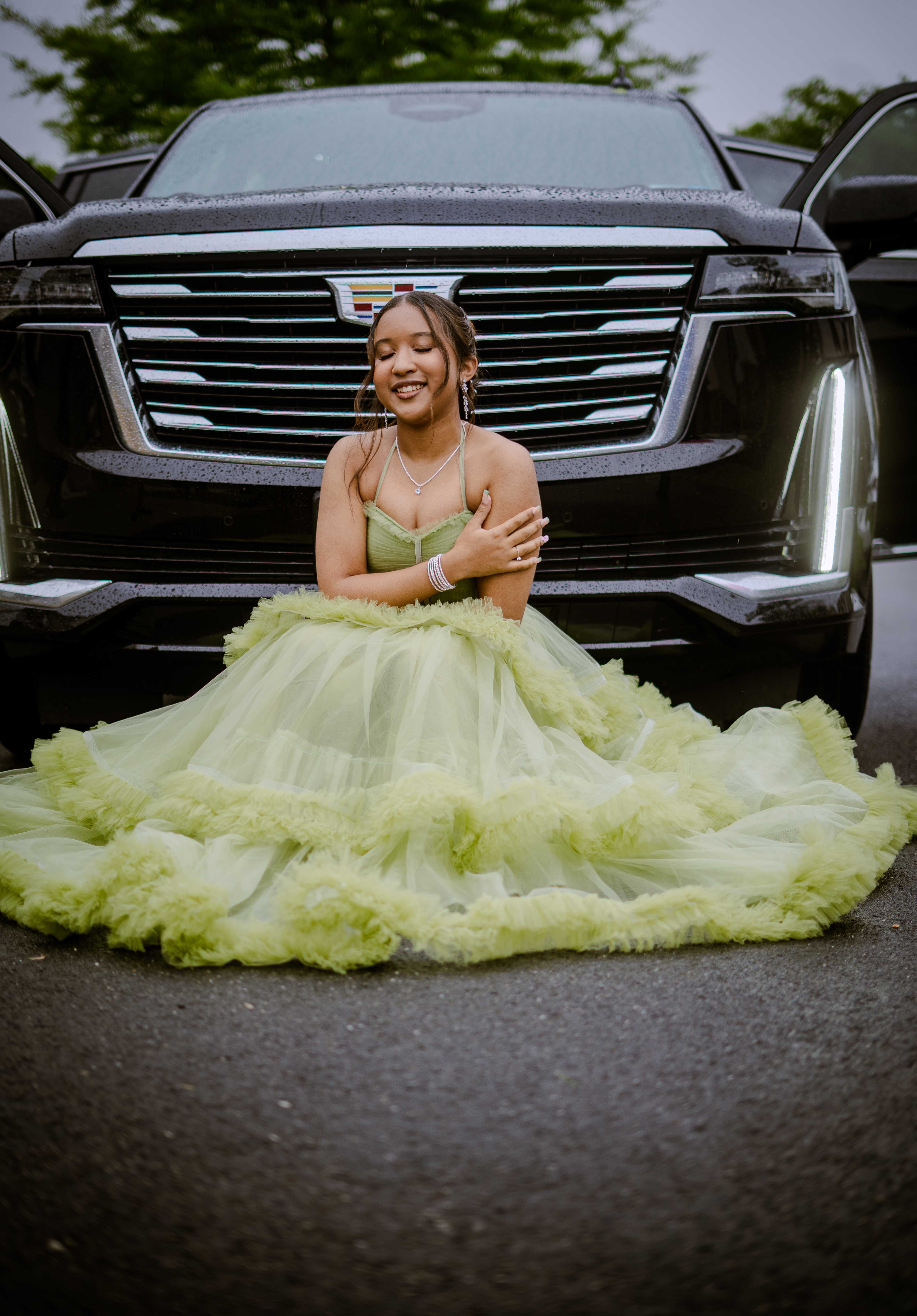 Graduate in mint green dress sitting by car